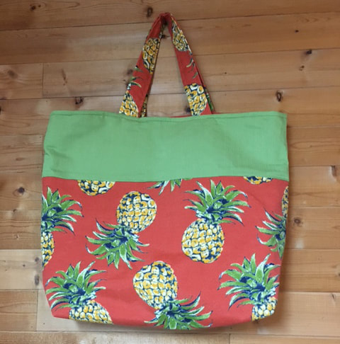 Patchwork fabric handbag made by local artist with strap and bottom showing pineapple design on orange background and wide light green upper band around top..